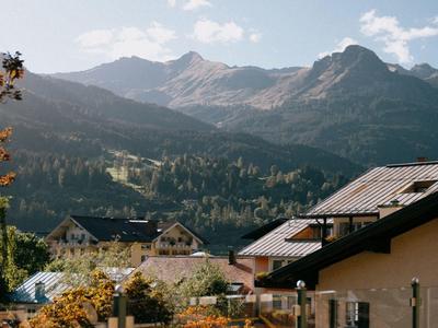 Blick auf Häuser mit Dächern vor bewaldeten Bergen unter klarem Himmel.