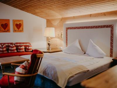 Gemütliches Hotelzimmer mit Holzbalkendecke, Doppelbett und Sofa mit roten Akzenten.