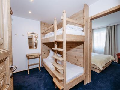 Schlafzimmer mit Holzetagenbett, Teppichboden, Kommode und angrenzendem Raum mit Doppelbett.