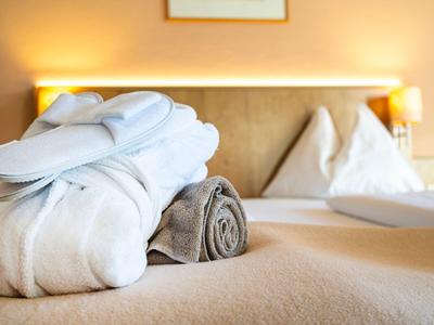 Frisch gefaltete Bademäntel liegen auf einem braunen Bett in einem Hotelzimmer.