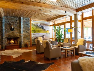 Gemütlicher Hotel-Loungebereich mit Kamin, Ledersesseln und großen Fenstern mit Bergblick.