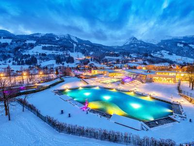 Beleuchtetes Freibad in verschneiter Winterlandschaft mit Bergen im Hintergrund bei Dämmerung.