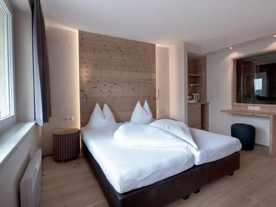 Camera d'hotel luminosa con letto matrimoniale, grande finestra e pavimento in legno.