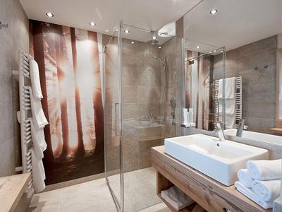 Bagno d'hotel moderno con doccia in vetro, grande specchio e doppi lavandini.