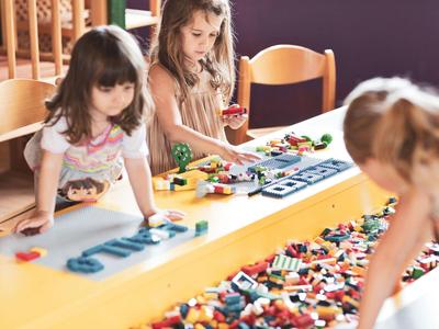 Bambini che giocano a un tavolo colorato in una stanza luminosa con sedie in legno.