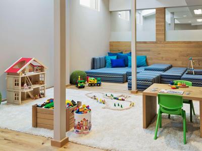Accogliente stanza giochi per bambini con giocattoli, moquette e posti a sedere in una stanza luminosa.