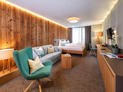 Modern eingerichtetes Hotelzimmer mit Holzwand, grünem Sessel, Bett und großem TV.