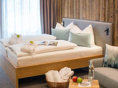 Modernes Schlafzimmer mit Holzwand, weißer Bettwäsche, zwei Kissen und Korb mit Handtüchern.