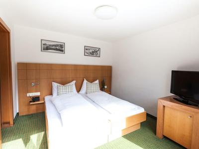 Helles Doppelzimmer mit zwei Betten, Holzmöbeln, grünem Teppich und Fernseher.