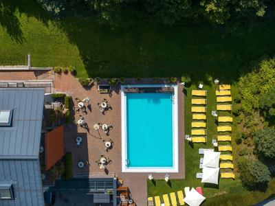 Luchtfoto van een hotel met een rechthoekig zwembad, ligstoelen en groene zones.