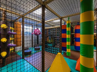 Bunter Indoorspielplatz mit Klettergerüst, Polstern und Netz umgeben.