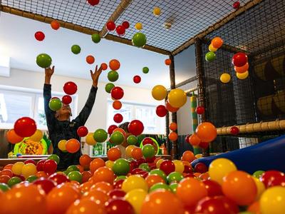 Kinder spielen in einem bunten Bällebad mit roten, orangefarbenen, gelben und grünen Kugeln.