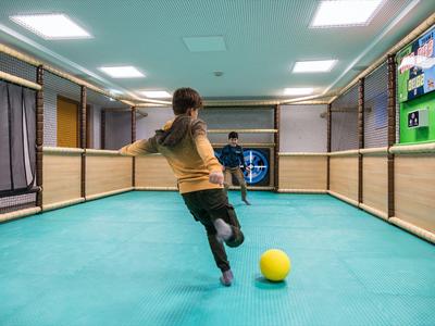 Ein Mädchen schießt in einer Halle mit grünem Boden einen gelben Ball in ein Tor.