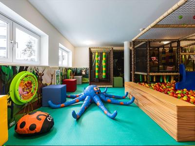 Innen-Spielbereich mit buntem Bodenkissen, Planschbecken, Ballgrube und Klettergerüst.