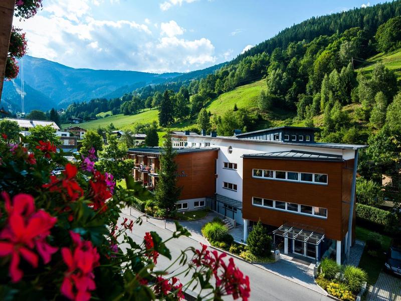 Moderne Gebäude vor grünen Bergen und blauem Himmel mit roten Blumen im Vordergrund.