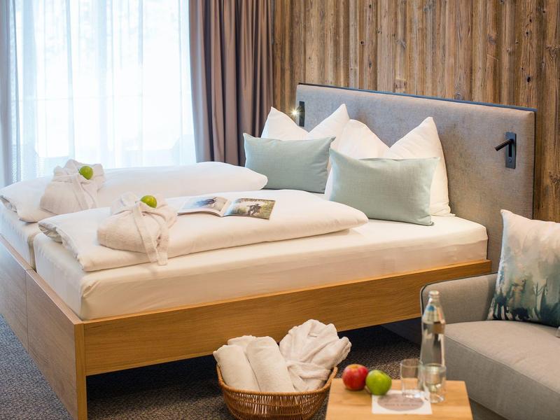 Modernes Schlafzimmer mit Holzwand, weißer Bettwäsche, zwei Kissen und Korb mit Handtüchern.