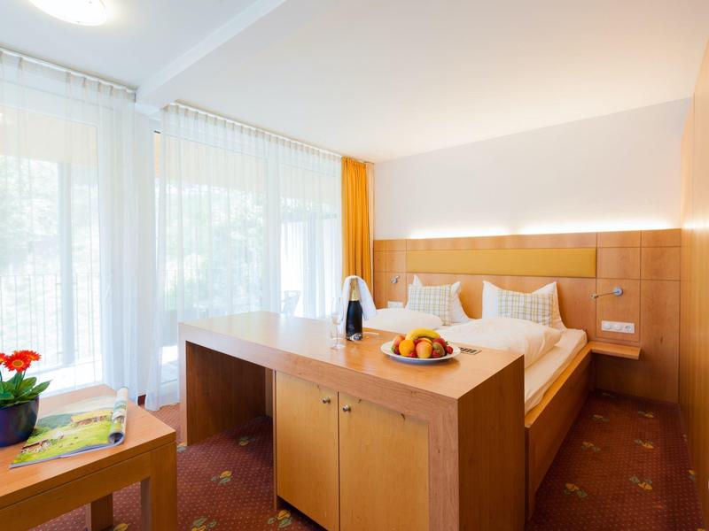 Modernes Hotelzimmer mit Doppelbett, Holzmöbeln, roten Teppich und großen Fenstern mit weißen Vorhängen.