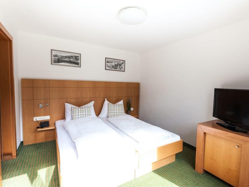 Helles Doppelzimmer mit zwei Betten, Holzmöbeln, grünem Teppich und Fernseher.