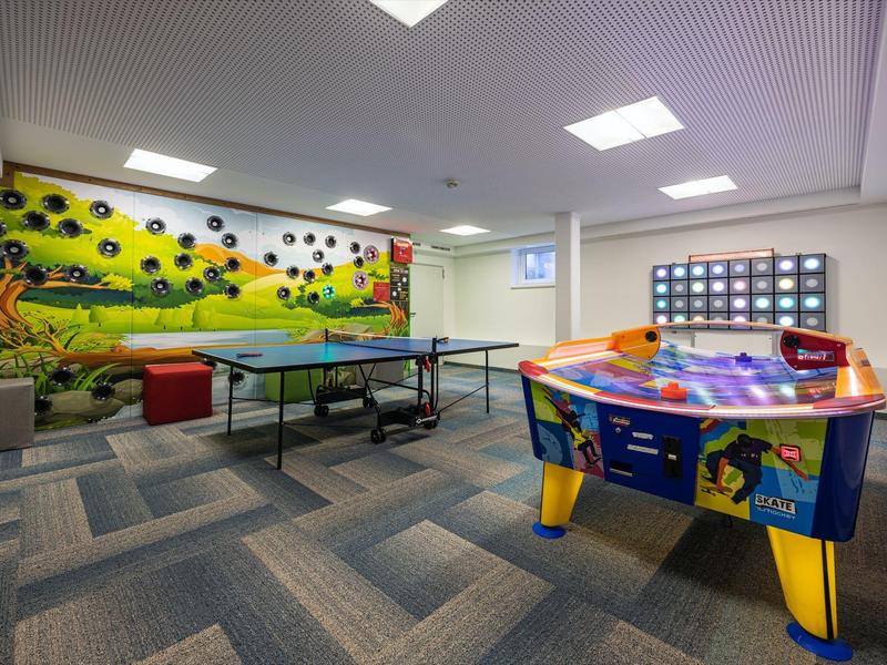 Spielzimmer mit Tischtennisplatte, Airhockeytisch, buntem Wandbild und grauem Teppichboden.