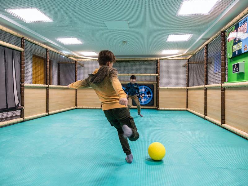 Ein Mädchen schießt in einer Halle mit grünem Boden einen gelben Ball in ein Tor.