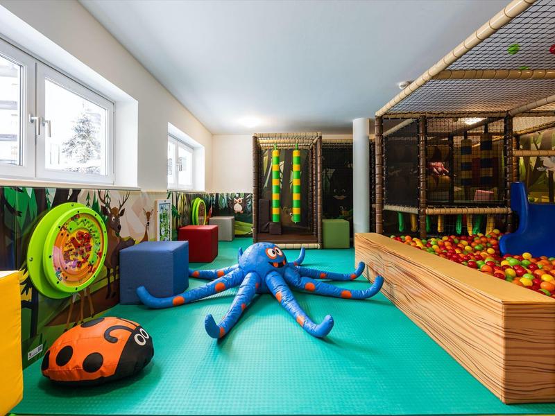 Innen-Spielbereich mit buntem Bodenkissen, Planschbecken, Ballgrube und Klettergerüst.