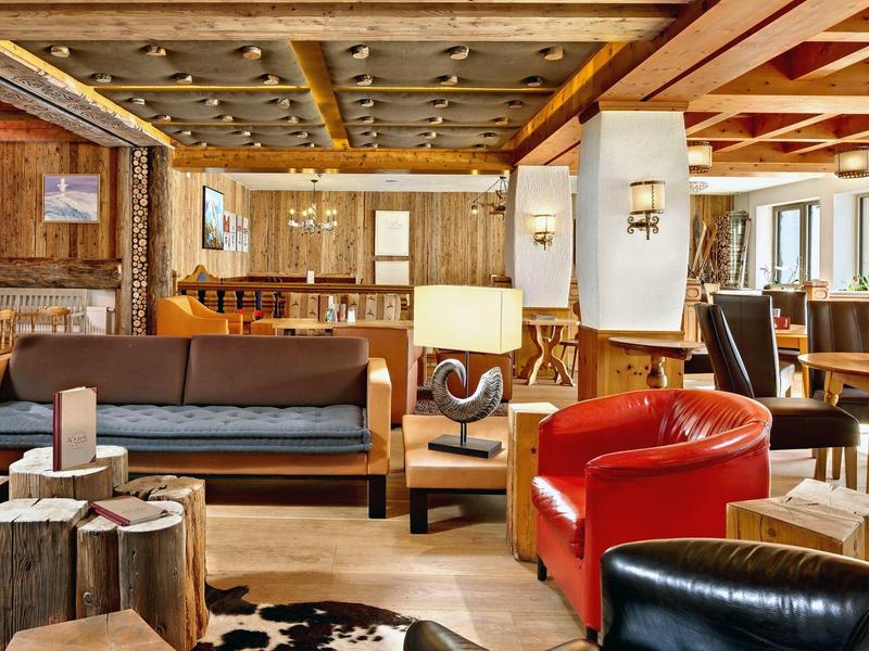 Gemütlicher Wohnbereich mit Holzmöbeln, roten Sesseln, Sofa und warmem Licht in rustikalem Stil.