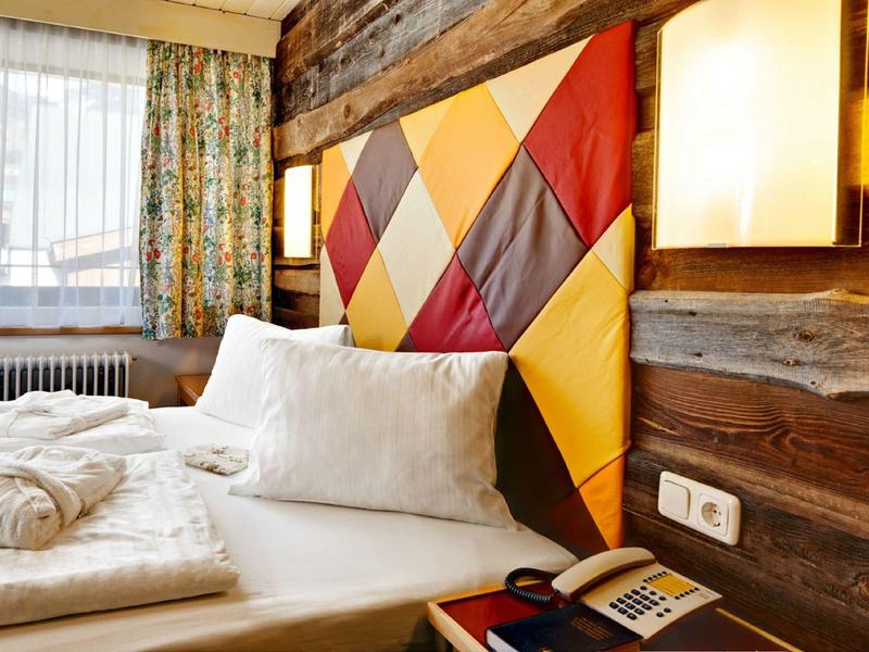 Gemütliches Schlafzimmer mit buntem, gemustertem Kopfteil und Holzwänden, hell beleuchtet.