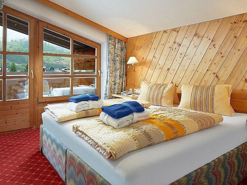 Gemütliches Schlafzimmer mit Holzwand, Doppelbett, buntem Teppich und Fenster zur Terrasse.