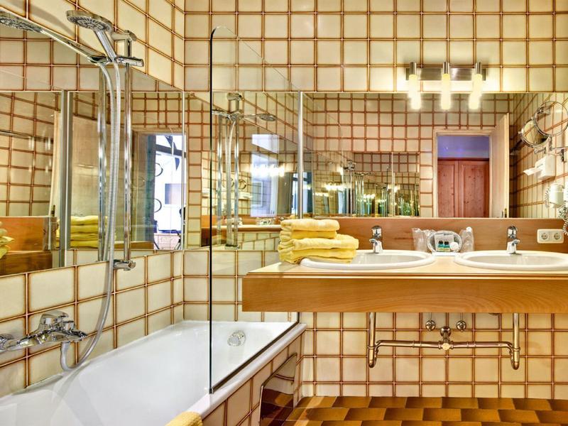 Innenraum eines Badezimmers mit gelben Fliesen, Badewanne, Waschbecken und Spiegel.