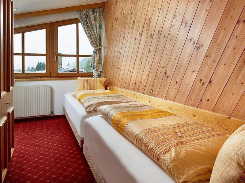 Gemütliches Schlafzimmer mit Holzverkleidung, zwei Betten, rotem Teppich und Fenster mit Vorhängen.