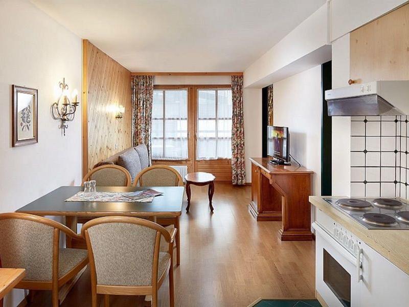 Helles Wohnzimmer mit Sofa, Holzmöbeln, Essbereich und offener Küche mit weißen Fliesen.