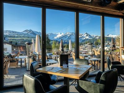 Interior de un restaurante con mesas, sillas y vista soleada a la montaña.