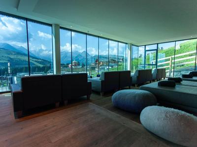 Área de descanso moderna con grandes ventanas panorámicas y vistas a la montaña en un hotel.
