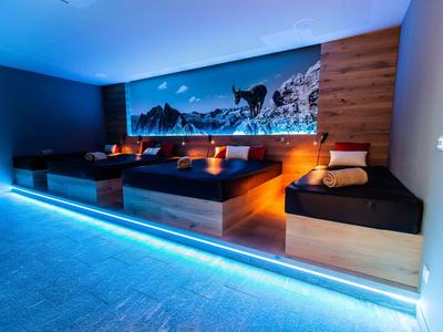 Dormitorio moderno con cuatro camas elevadas, revestimiento de madera y luz LED azul en el suelo.