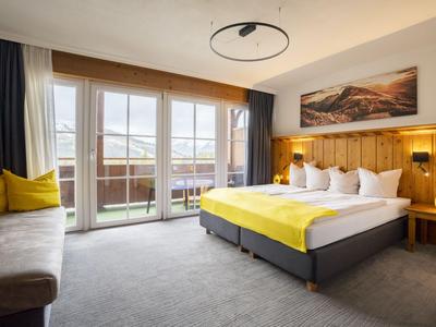 Habitación de hotel luminosa con cama doble grande, detalles amarillos y balcón con vista.