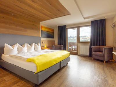 Habitación de hotel moderna con cama grande, manta amarilla y balcón con vista.