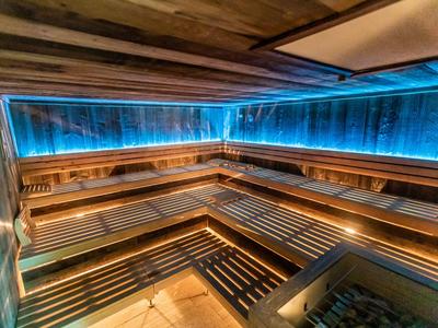 Sauna moderna con bancos de madera y luz LED azul en las paredes.
