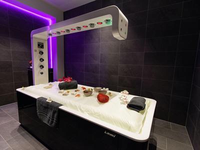 Sala moderna de masaje o tratamiento con mesa iluminada y paredes negras.