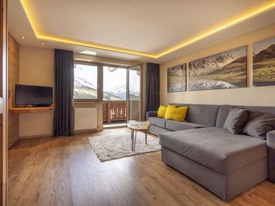 Sala acogedora con gran sofá esquinero, televisor y balcón con vistas a la montaña.