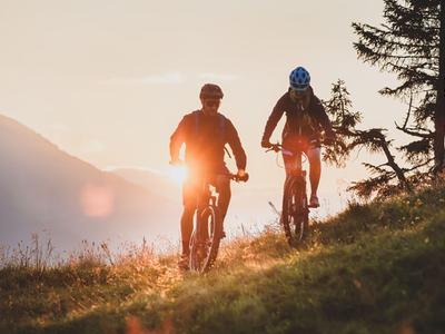 Two people riding mountain bikes at sunset on a hill.
