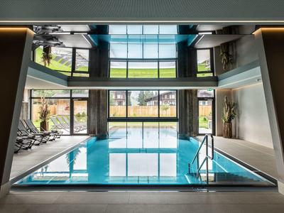 Moderner Innenpool mit glattem Wasser, großen Fenstern und Liegestühlen nebenan.