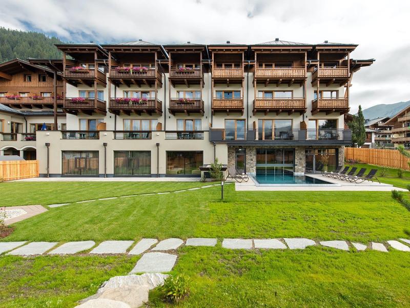 Großes mehrstöckiges Holzhaus mit Balkon, moderner Pool und grüner Rasenfläche im Vordergrund.