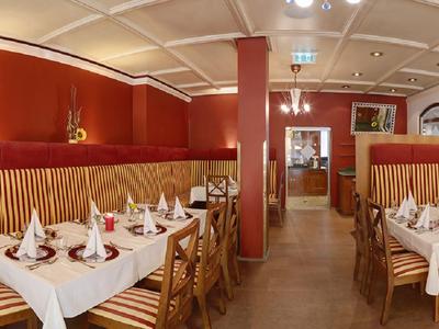 Elegant restaurant met rood-gouden wanddecoratie en gedekte tafels.