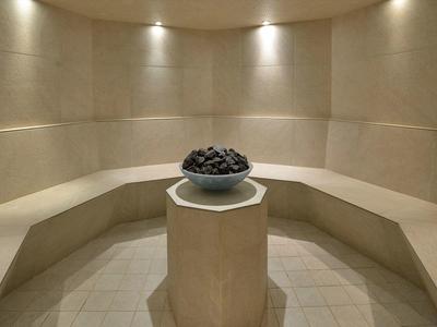 Runder, heller Sauna-Raum mit gebogenen Sitzen und einem Steintopf auf einem zentralen Podest.