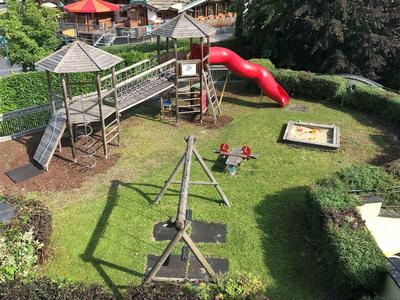 Kinderspielplatz mit Rutsche, Wippe, Sandkasten und Klettergerüst auf grüner Wiese.