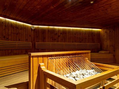 Holzsauna mit Sitzbänken und einem Steinkamin zur Wärmeverteilung, warmes Licht an der Decke.