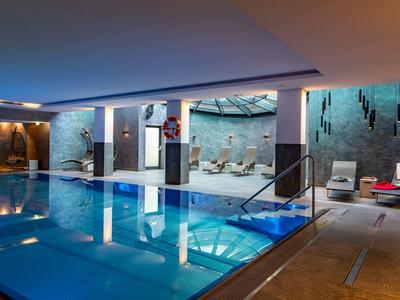 Innenpool mit bläulichem Wasser, Lounge-Bereichen, Liegestühlen und moderner Beleuchtung.