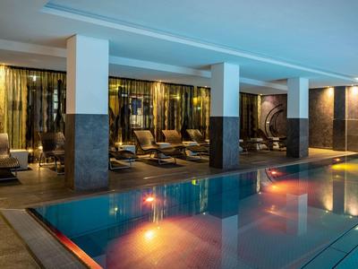 Moderner Innenpool mit blauer Wasserfläche, bequemen Liegen und warmem Lichtambiente.