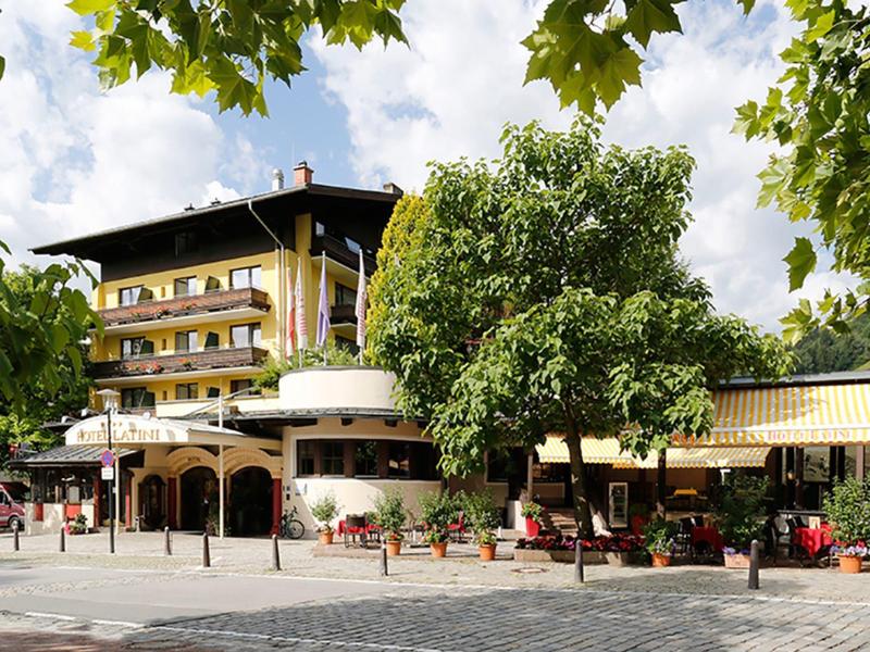 Mehrstöckiges Gebäude mit Balkonen in warmen Farben, umgeben von Bäumen und Sitzplätzen im Freien.