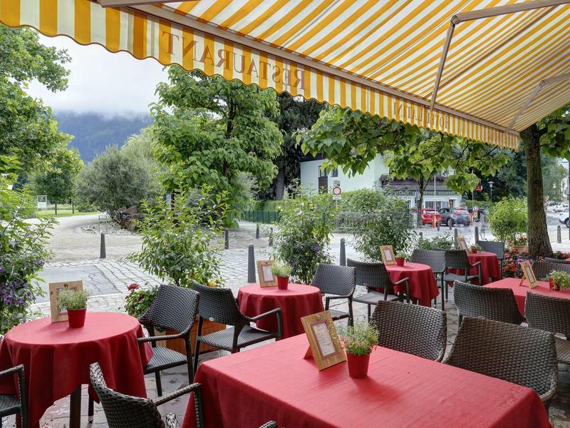 Außenbereich eines Cafés mit roten Tischdecken, schwarzen Stühlen und gelb-weißer Markise.